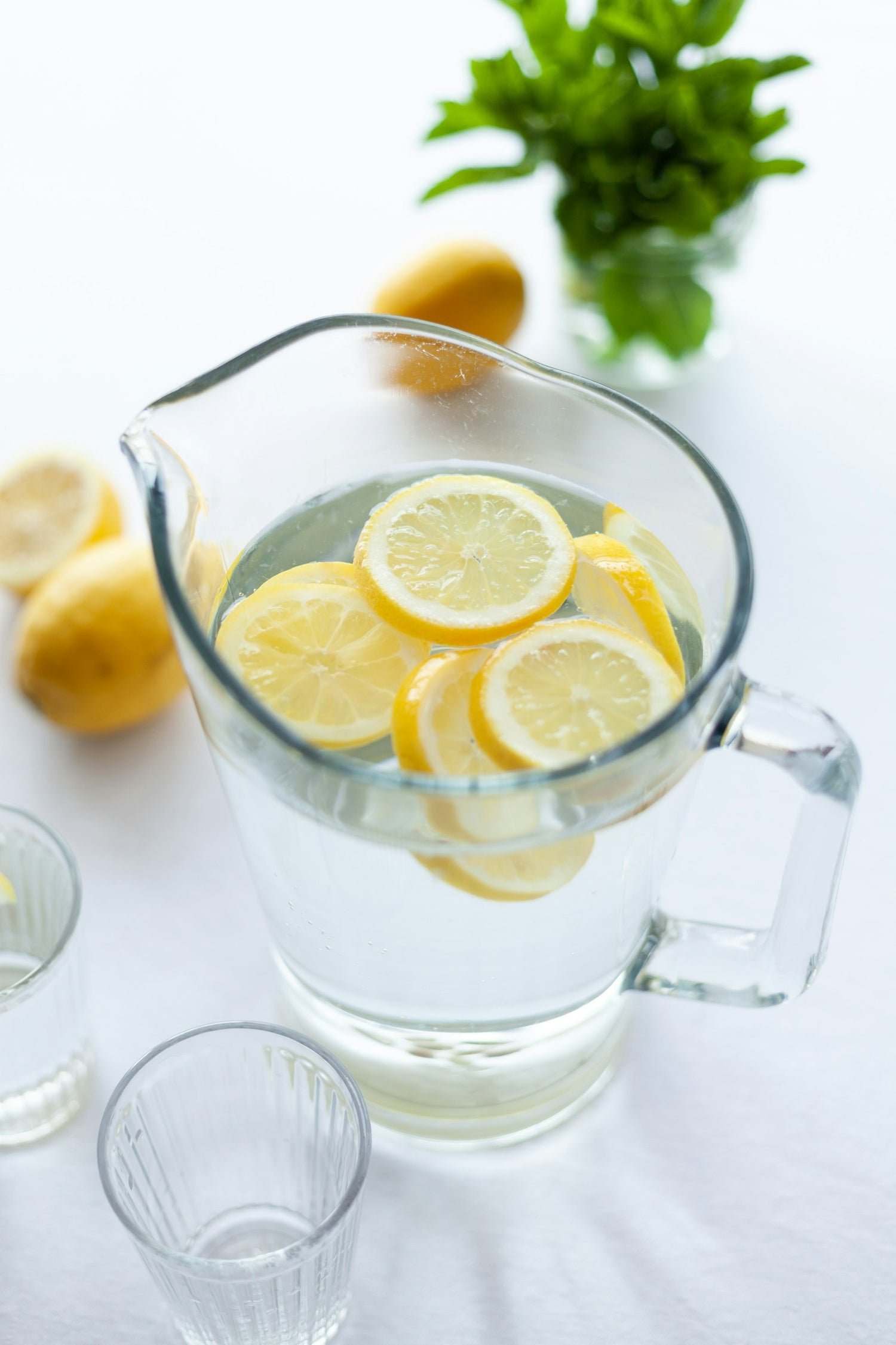 Glass pitcher of water with lemon slices on a bright white surface, illustrating hydration and electrolytes for workouts