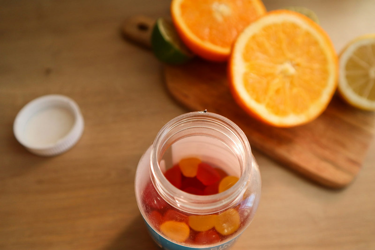 Jar of gummy sweets beside sliced oranges, illustrating creatine gummies vs powder