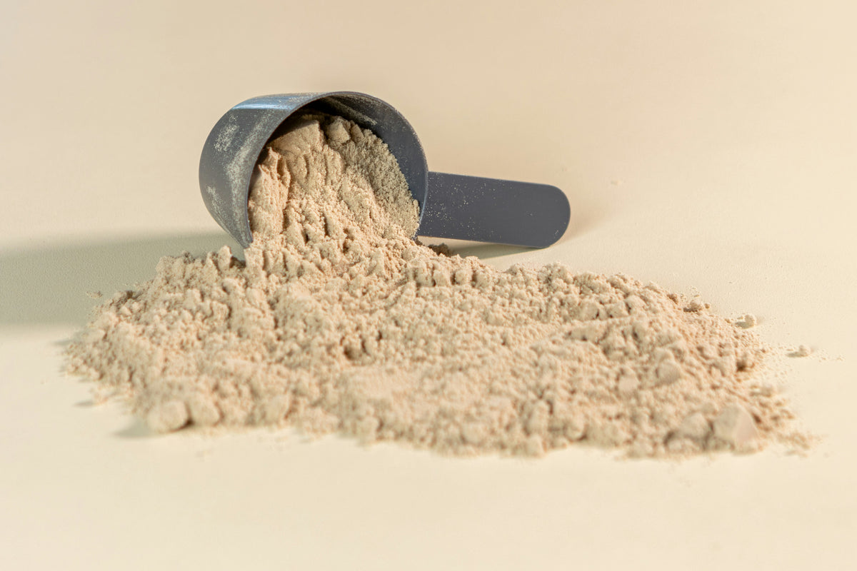 A scoop tipped over with amino acid powder spilling onto a light surface