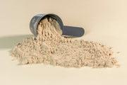 A scoop tipped over with amino acid powder spilling onto a light surface